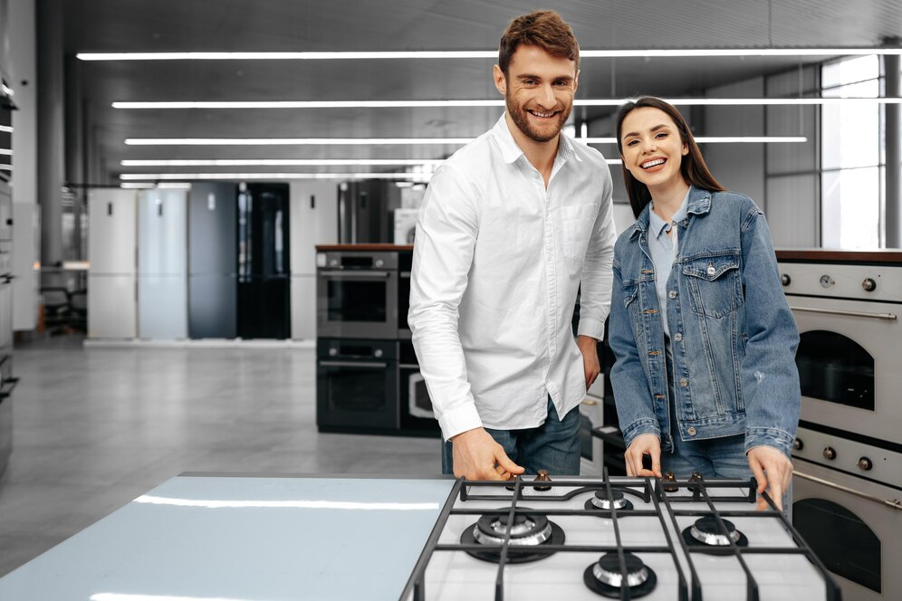 A smiling couple standing in a store with new household appliances, looking excited about their recent purchase